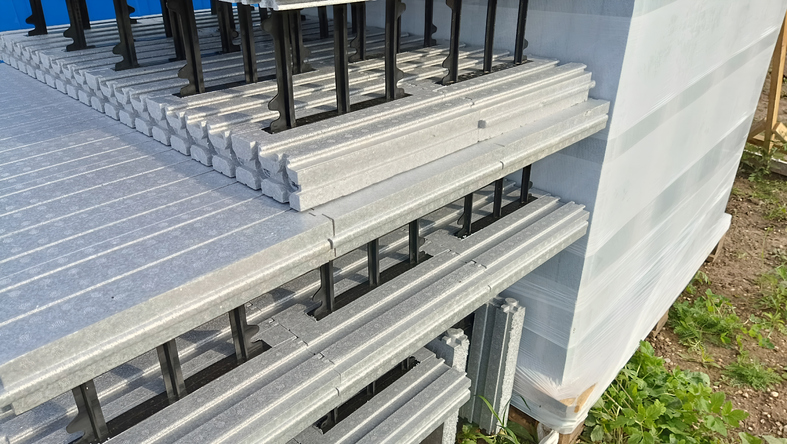 Close-up of lightweight grey concrete insulating formwork blocks. Stacks of construction materials featuring black plastic connectors and an interlocking design. ICF polystyrene building block.